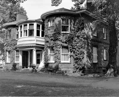 Corner view of the Fairholm villa showing the mottled red brick walls; and cut stone used as lintels over the windows, for the raised basement, and as a string course between the two storeys. © Parks Canada Agency / Agence Parcs Canada, n.d.