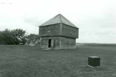 General view of the Blockhouse, showing its simple, compact two-storey massing with an overhanging second floor and medium-pitched kingpost roof structure clad in wood shingles, 1992. (© Agence Parcs Canada / Parks Canada Agency, 1992.)