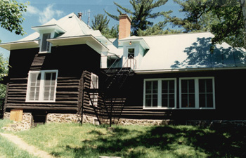 South view of Wabenaki Lodge, showing the hip roof with upturned eaves, hipped dormers, and the brick chimney, 1990. © Canadian Parks Services / Service canadien des parcs, 1990.