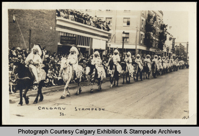 Spectators line the street as Indians in feather headdresses ride in single file in the Stampede Parade, date unknown (1925-1935?) © Calgary Exhibition & Stampede Archives