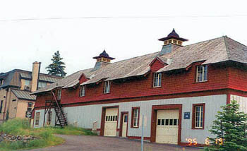Corner view of the north elevation of the Service Building showing the shingled hip roof with a broad overhang and carved brackets, decorated roof ventilators, dormers and cut-away eaves over the windows, 1995. © Parks Canada Agency / Agence Parcs Canada, C. Zacconi, 1995.