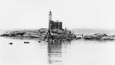 View of the back side of Fisgard lighstation during the Second World War, showing buoys holding up the submarine net. The balcony above the back door is visible on the left side of the image . © PAC, DND, RCN E-3194
