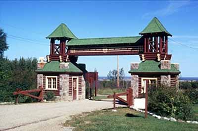 General view of the Riding Mountain Park East Gate Registration Complex's East Gate Entrance Building, showing its design as a truss bridge stretching across the road, 1973 © Parks Canada Agency / Agence Parcs Canada, P. McCloskey, 1973