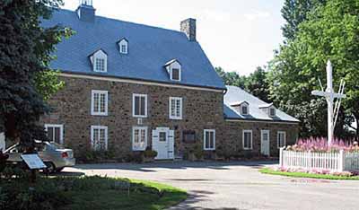 Exterior view of Maison Saint-Gabriel, showing the east lean-to and the wooden cross, 2005. © Parks Canada Agency / Agence Parcs Canada, N. Clerk, 2005.