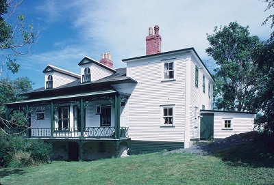 Rear facade showing its deep verandah on three sides with bellcast roof and decorative wooden fretwork, and its generous bay and French windows. © Parks Canada Agency / Agence Parcs Canada