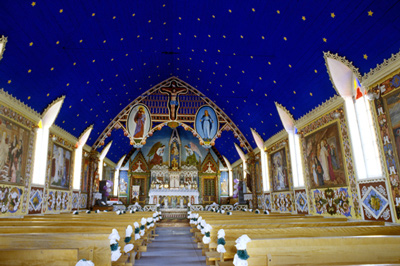 View of the interior of the Church of Our Lady of Good Hope emphasizing the Gothic style painted decoration of interior, including ornamentation surrounding figural panels and ornamented wainscotting, painted floor, painted tripartite arch motif at altar. © Parks Canada Agency / Agence Parcs Canada, n.d.