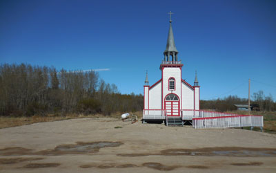 General view of St. Peter’s Anglican Church, showing the rectangular massing with a gable-ended, pitched roof and a porch of smaller but similar form surmounted by a belfry. © Hay River Dene Band / Bande des Dénés de Hay River.