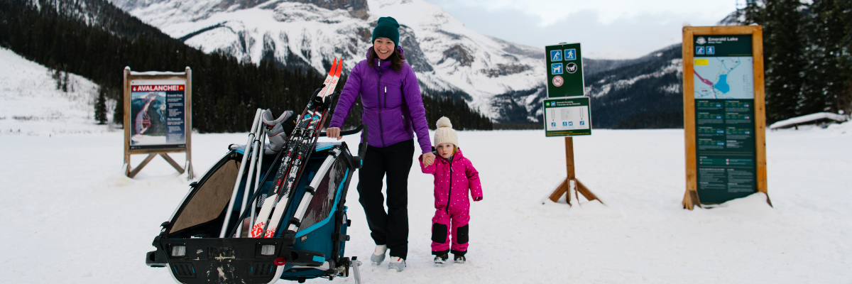 Un parent tient la main de son enfant tandis qu’il pousse un chariot chargée d'équipement de ski de randonnée sur le lac Emerald.