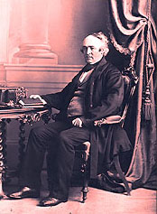 A picture of Mr. John McDougall sitting on a sofa near a table and holding a book in his right hand He was the owner of the Forges from 1863 until 1876. 