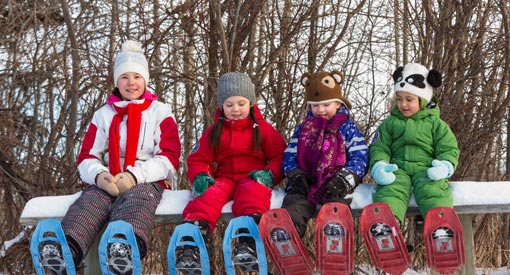 Happy children sitting on a bench with snowshoes in their feet during winter.