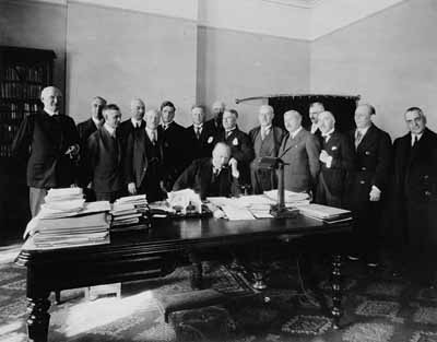 Rt. Hon. R.B. Bennett, Prime Minister of Canada, surrounded by members of the Cabinet, speaking by telephone to Sir George Perley at the British Empire Trade Fair at Buenos Aires.  Date: 13 Mar. 1931 © National Film Board of Canada. Photothèque Bibliothèque et Archives Canada / Library and Archives Canada / C-009076