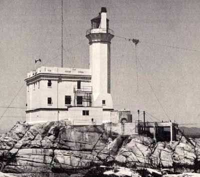 General view of the exterior of the Light Tower, showing its form and massing which consist of a tall, slightly tapered octagonal tower with narrow slit openings, flared lantern platform, lantern and light. © Parks Canada Agency / Agence Parcs Canada