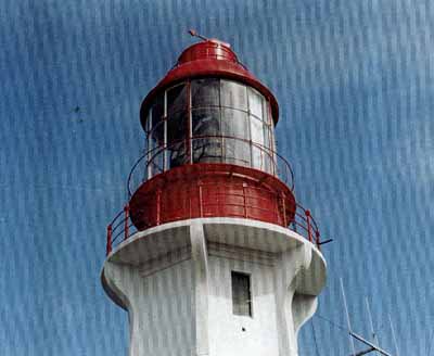 Vue en détail du phare, où l'on peut apercevoir la lanterne cylindrique en métal, surmontée d’un aérateur en dôme et d’une girouette, 1994. © Canadian Coast Guard / Garde côtière canadienne, 1994.
