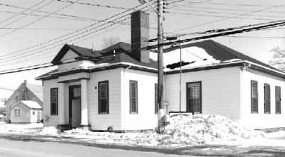Corner view of the Armoury at Middleton, showing a low profile hipped roof and central portico, 1993. © Department of National Defence / Ministère de la Défense nationale, 1993.