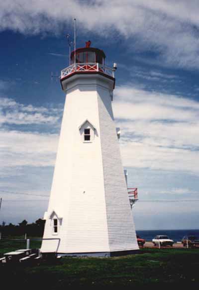 Vue de l'extérieur de la tour, qui montre la lanterne en acier peint en rouge proportionnée à la tour et le garde-fou caractéristique à croisillons en bois, 1990. © Transport Canada / Transports Canada, 1990.