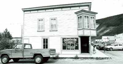 View of the main entrance to Harrington's Store (15), showing the square-sided oriel window placed at the salient angle, the richly ornamented double front door, and the painted cove siding, 1987. © Department of the Environment / Ministère de l'Environnement, 1987.