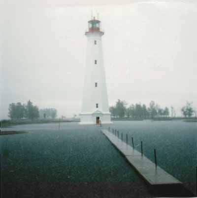 General view of the Light Tower, showing the building’s form and massing, tall profile and flared platform topped by an iron lantern, 1986. © Canadian Coast Guard / Garde côtière canadienne, 1986.