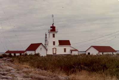 Side view of the Lighthouse and Dwelling on Gereaux Island, showing the three-storey, square, tapered form of the tower and the attached gable-roofed dwelling that is well integrated with the tower, 1981. © Parks Canada Agency / Agence Parcs Canada, 1981.