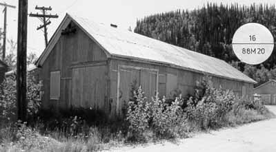 Corner view of the Garage and Fire Hall, showing its rectangular shape, its gable roof, its corrugated metal siding and roof covering, and its wood-frame structure, 1988. (© Parks Canada Agency / Agence Parcs Canada, 1988.)