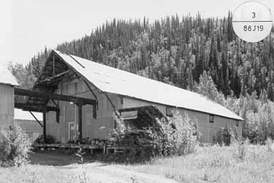 Corner view of Warehouse 2, showing the building’s simple, warehouse form and massing including the gable roof, 1988. (© Agence Parcs Canada / Parks Canada Agency, 1988.)