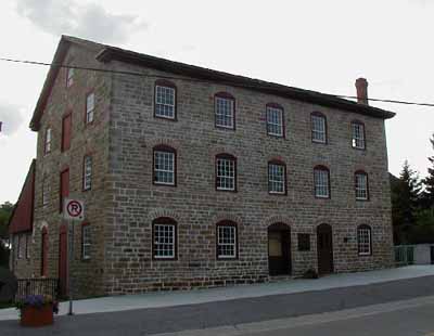 General view of the Old Stone Mill, showing its neo-classical, exterior detailing, including its bays trimmed with graceful, segmentally arched, stone voussoirs, 2004. © Parks Canada Agency / Agence Parcs Canada, 2004.