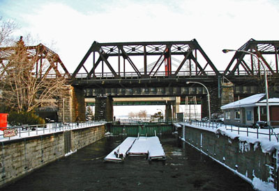 General view of Sainte-Anne-de-Bellevue Canal, showing the entrance walls above and below the lock, and the stone masonry coping of the lock walls, 2003. © Parks Canada Agency / Agence Parcs Canada, 2003.