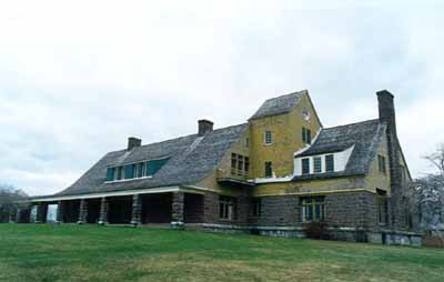 View of the façade of the Main House, showing Shingle styling and its roofline interrupted by a single dormer and deep front porch the length of the building’s central core, 1995. (© Parks canada Agency/ Agence Parcs Canada, L. Maitland, 1995.)