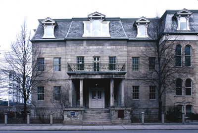 Facade of the Bank of Upper Canada Building showing the Neoclassical portico, consisting of: a raised podium; paired columns; a strongly defined entablature; and a second-storey balcony. © Parks Canada \ Parcs Canada, n.d.