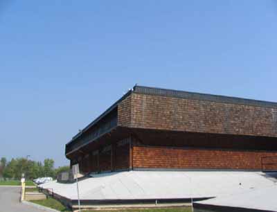 Vue de l'extérieur du bloc 1800, qui montre le parement en bardeaux de bois ainsi que la base pyramidale avec un toit en surplomb lourd en forme de boîte, 2005. © Parks Canada Agency / Agence Parcs Canada, Kate MacFarlane, 2005.