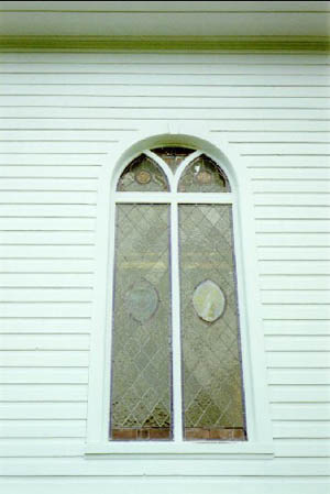 Detail of St. Peter's Anglican Church, showing a stained glass window and the white wooden planking, 1992. © Agence Parcs Canada / Parks Canada Agency, André Charbonneau, 1992.