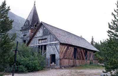 Corner view of St. Andrew's Presbyterian Church, showing its simple rectangular wood frame structure with a gable roof and an adjoining asymmetrically placed tower, 1988. © Parks Canada Agency/Agence Parcs Canada, Chilkoot Trail National Historic Park, 1988.