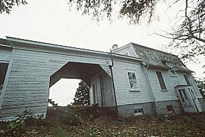General view of Building 43, showing a covered passageway that connects a mansard roofed one-storey residence to a gable roofed shed, circa 2004. © Parks Canada Agency / Agence Parcs Canada, circa / vers 2004.