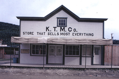 General view of the KTM Building, showing the painted, decorative, two-and-a-half-bay-retail façade with large retail windows, double entrance door and single door to the side, and its irregular arrangement of large retail windows, 1987. © Agence Parcs Canada / Parks Canada Agency, 1987.