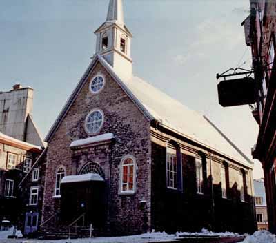 Vue en angle montrant la façade principale du lieu historique national du Canada de l'Église Notre-Dame-des-Victoires, 1988. © Agence Parcs Canada / Parks Canada Agency, Architectural History Branch, 1988.