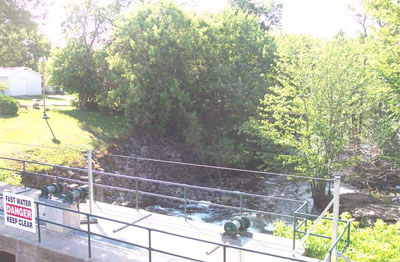 View of the east bank of the Gananoque River from the bridge. The designated place lies in the treed area in the centre of the photo © Parks Canada Agency / Agence Parcs Canada, 2005, (Heritage Research Associates Inc.)
