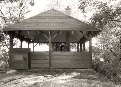 General view of the Adelaide Island Picnic Shelter, showing the hipped roof, exposed rafters, vertical wood support posts and wood brackets, 1992. © Parks Canada Agency / Agence Parcs Canada / Historica Resources Ltd., 1992.