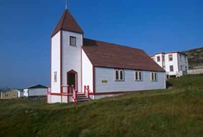 General view of Battle Harbour Historic District, St. James the Apostle Anglican Church with its rectangular, gable-roofed massing, clapboarding, two-stories and pyramidal tower, 2003. © Parks Canada Agency/Agence Parcs Canada, J. McQuarrie, 2003.