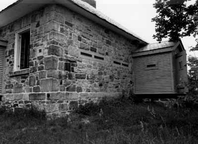 Vue en angle de la résidence fortifiée du maître-éclusier de Jones Falls, qui montre le porche fortifié, 1989. © Parks Canada Agency / Agence Parcs Canada, 1989.