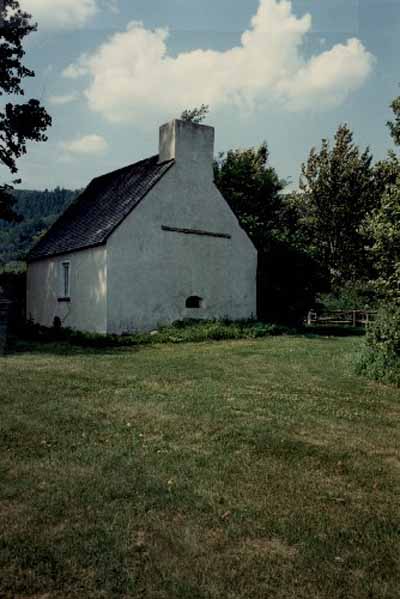 Rear view of the French People's House, showing its high gable roof and its large chimney with an integrated, outdoors wood-buring oven, 1991. © Parks Canada Agency / Agence Parcs Canada, Christine Chartré, 1991.