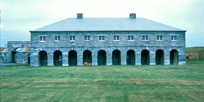 General view of Fort Lennox showing the buildings, their stone construction, their volume, mass, roof type, window and door placements. © Parks Canada Agency / Agence Parcs Canada.