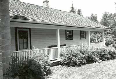 Façade of the Defensible Lockmaster's House, showing the single-storey clapboard addition with full-length verandah, 1989. © Parks Canada Agency / Agence Parcs Canada, Couture, 1989.
