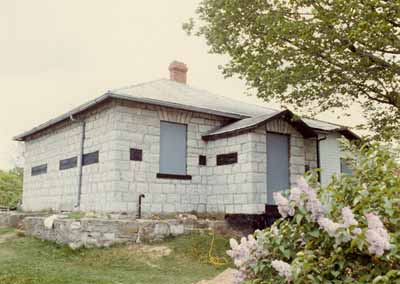 Vue générale de la façade ouest de la maison fortifiée du maître-éclusier, 1987. © Parks Canada Agency / Agence Parcs Canada, 1987.