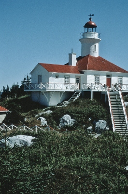 General view of the lighthouse cylindrical tower, clad with painted metal panels, rising out of the wooden square building © Agence Parcs Canada | Parks Canada Agency, Jean-François Bergeron.
