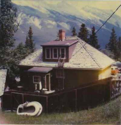 Rear view of the Upper Hot Pool Residence, showing its one-and-a-half storey structure of standard platform frame construction, with a rectangular plan and medium-pitch gable roof, 1990. © Parks Canada Agency / Agence Parks Canada, 1990.