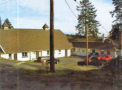 General view of the Cow Barn and Dairy showing its barn roofs with their wide eaves, exposed rafters, ventilation cupolas, external chimneys, and shed dormer windows, 2000. © Department of National Defence / Ministère de la Défense nationale, D. Cebula, 2000.