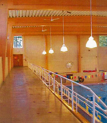 General view of the interior of the Swimming Pool RR22A showing the successful integration of traditional wood elements such as the glue laminated timbers with modern masonry elements such as the concrete surfaces and tile wainscoting, 2000. © Department of National Defence / Ministère de la Défense nationale, 2000.