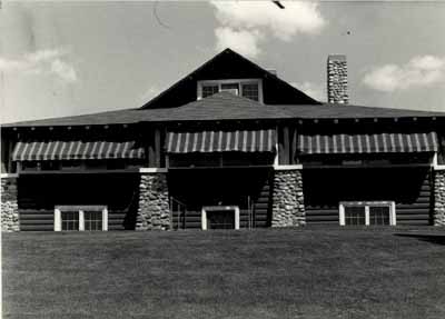 General view of the Golf Clubhouse (B7), showing the horizontal log construction and the cobblestone detailing, 1984. © Agence Parcs Canada / Parks Canada Agency, 1984.