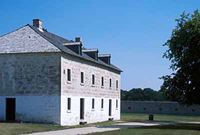 Corner view of the Warehouse showing the medium-pitched hipped roof with gabled dormers and two stone chimneys and the arrangement of windows and doors, 2003. © Parks Canada Agency / Agence Parcs Canada, G. Kopelow, 2003.