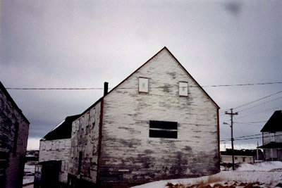 Northwest façade of the Ryan Store and Fish Purchasing Centre, showing the two-storey, box-like form capped with a side-gable roof, 1993. © Agence Parcs Canada / Parks Canada Agency, 1993.