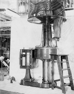 Historic photograph taken in New Férolle Peninsula Lighthouse showing a man working in the lense. © Library and Archives, Department of Transports, Marine Aids Division | Bibliothèque et Archives Canada, ministère des Transports, division des aides maritimes, e0003719347.